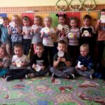 na zdjęciu widać stojące i siedzące dzieci w sali przedszkolnej trzymające papierowe kurczaki