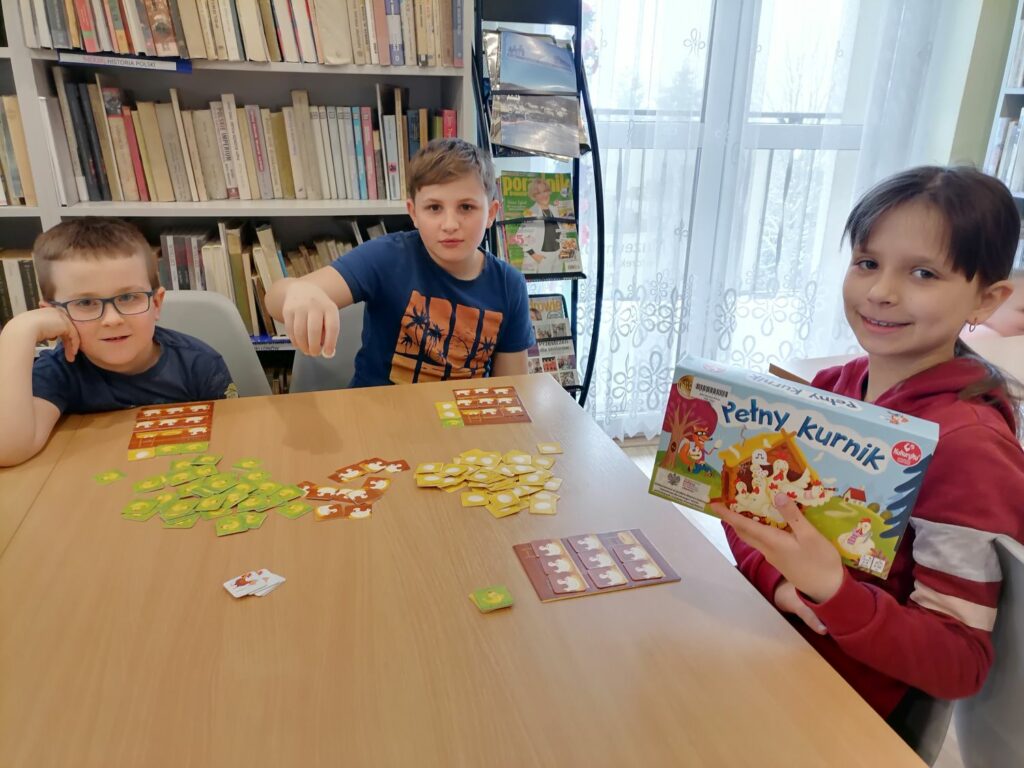 Na zdjęciu widocznych jest troje dzieci (2 chłopców i 1 dziewczynka) grających w grę pełny kurnik.