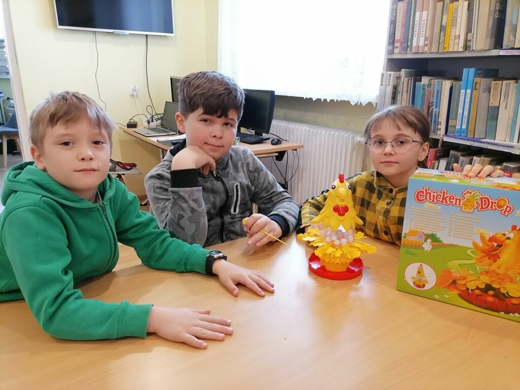 Na zdjęciu widocznych jest troje dzieci (2 chłopców i 1 dziewczynka) grających w grę Chicken drop.