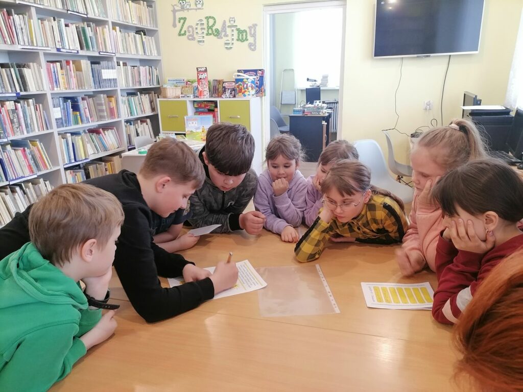 Na zdjęciu widoczna jest grupa dzieci (3 chłopców i 5 dziewczynek) podczas zabawy w wielkanocne podchody i rozwiązywania jednego z zadań.