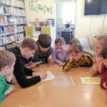 Na zdjęciu widoczna jest grupa dzieci (3 chłopców i 5 dziewczynek) podczas zabawy w wielkanocne podchody i rozwiązywania jednego z zadań.