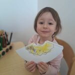 dziewczynka siedzi na krześle i trzyma w ręku pracę plastyczną