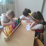 trzy dziewczynki siedzą przy stoliku i rysują kredkami
