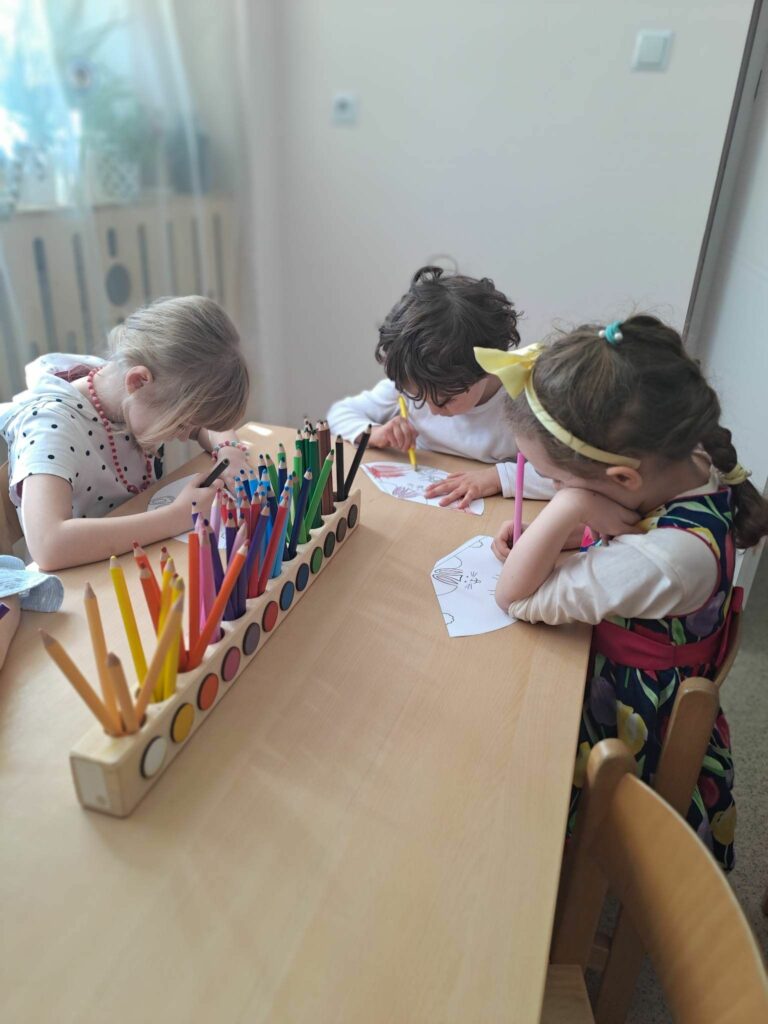 trzy dziewczynki siedzą przy stoliku i rysują kredkami