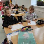 na zdjęciu widać salę szkolną, przy stolikach siedzą dzieci wykonują rysunki