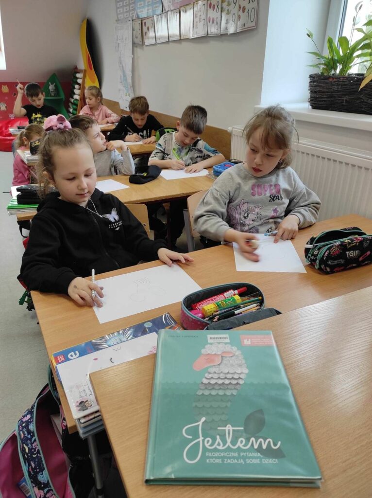 na zdjęciu widać salę szkolną, przy stolikach siedzą dzieci wykonują rysunki