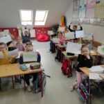 na zdjęciu widać salę szkolną, przy stolikach siedzą dzieci prezentują swoje rysunki