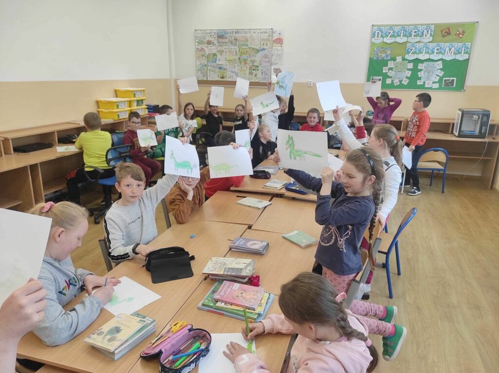 na zdjęciu widać salę szkolną, przy stołach siedzą dzieci, bibliotekarz czyta list skierowany do dzieci