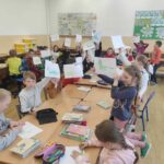 na zdjęciu widać salę szkolną, przy stołach siedzą dzieci, bibliotekarz czyta list skierowany do dzieci