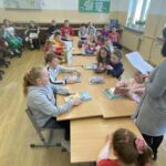 na zdjęciu widać salę szkolną, przy stołach siedzą dzieci, bibliotekarz czyta list skierowany do dzieci