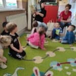 na zdjęciu widać salę przedszkolną, dzieci siedzą na dywanie, bibliotekarz czyta książkę