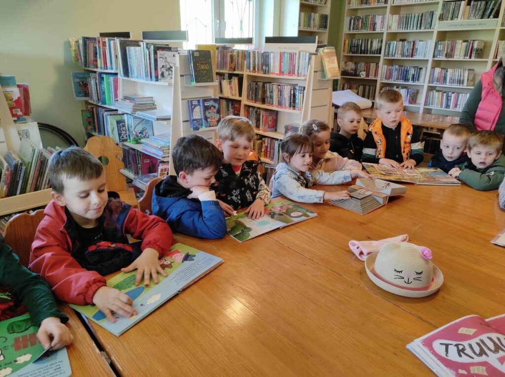 Na zdjęciu widać dzieci, siedzą przy stole, oglądają książeczki