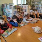 Na zdjęciu widać dzieci, siedzą przy stole, oglądają książeczki