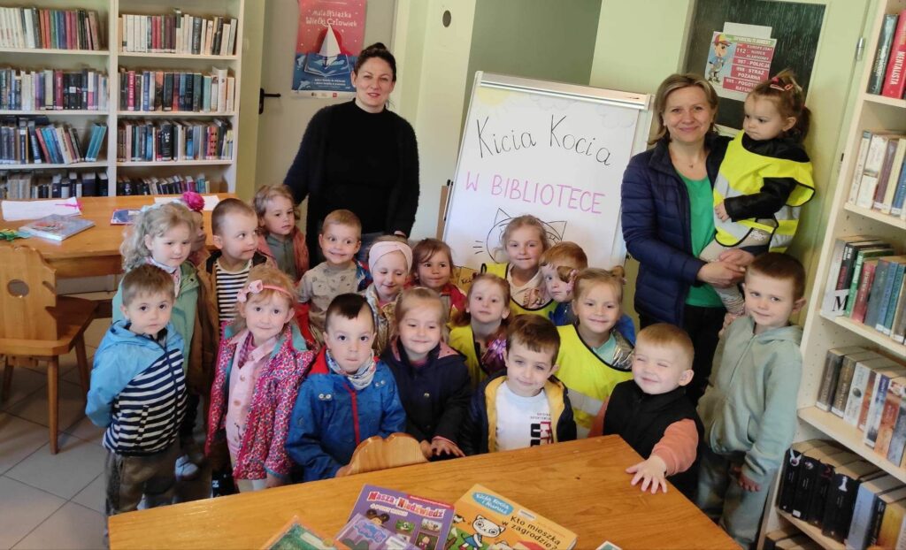 Na zdjęciu widać salę biblioteczną, na zdjęciu widać dzieci odwiedzające bibliotekę, wychowawcę przedszkolnego i bibliotekarza