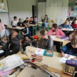 na zdjęciu widać salę szkolną, przy stolikach siedzą dzieci, uzupełnią karty pracy