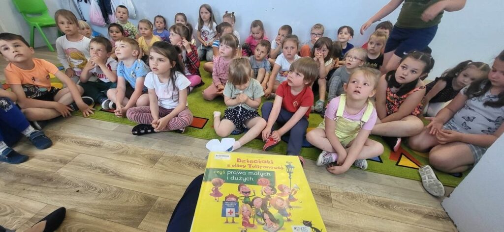 na zdjęciu widać siedzące dzieci a przed nimi książkę.