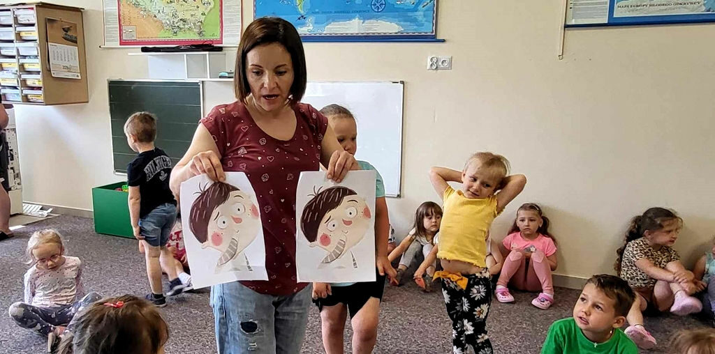na zdjęciu widać bibliotekarkę pokazującą dzieciom ilustracje