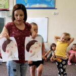 na zdjęciu widać bibliotekarkę pokazującą dzieciom ilustracje