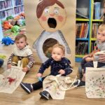 na zdjęciu widać sale biblioteczna oraz małe dzieci wraz z mamami siedzących na podłodze.