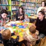 na zdjęciu widać dzieci i mamy siedzące przy stoliku w bibliotecznej sali