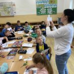 na zdjęciu widać salę szkolną, dzieci siedzą wokół stołu, wykonują pracę plastyczną