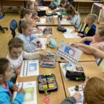na zdjęciu widać salę szkolną, dzieci siedzą wokół stołu, wykonują pracę plastyczną