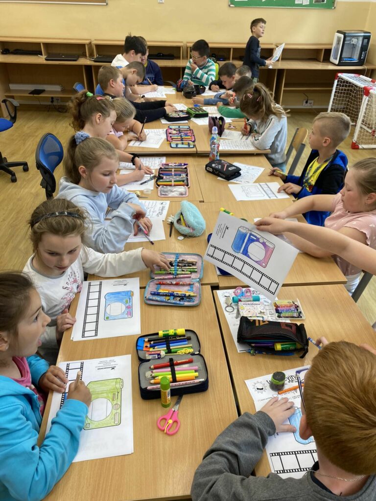 na zdjęciu widać salę szkolną, dzieci siedzą wokół stołu, wykonują pracę plastyczną