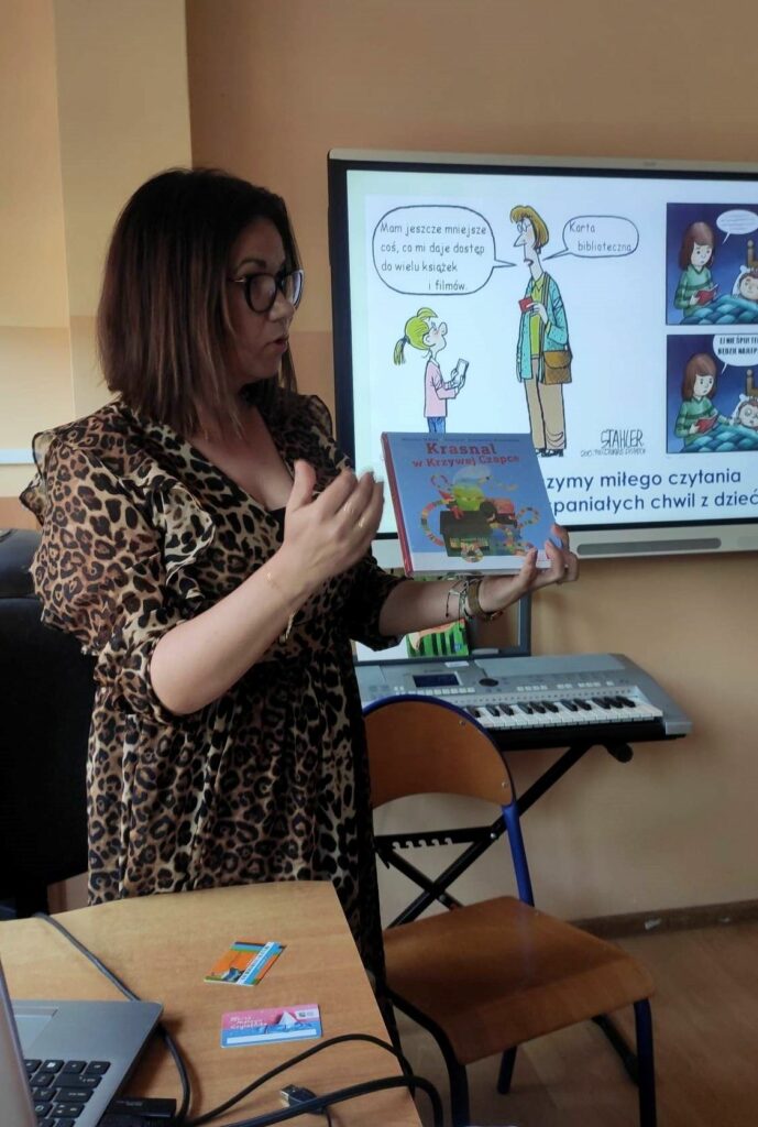 na zdjęciu widać kobietę bibliotekarkę stojąca z książką w ręku