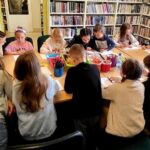 na zdjęciu widać dzieci siedzące wokół stołu w sali bibliotecznej