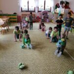 Na zdjęciu widoczna jest grupa przedszkolaków biorących udział w żółwiowych wyścigach polegających na przenoszeniu na plecach woreczków wokół przeszkód tak by ich nie upuścić.