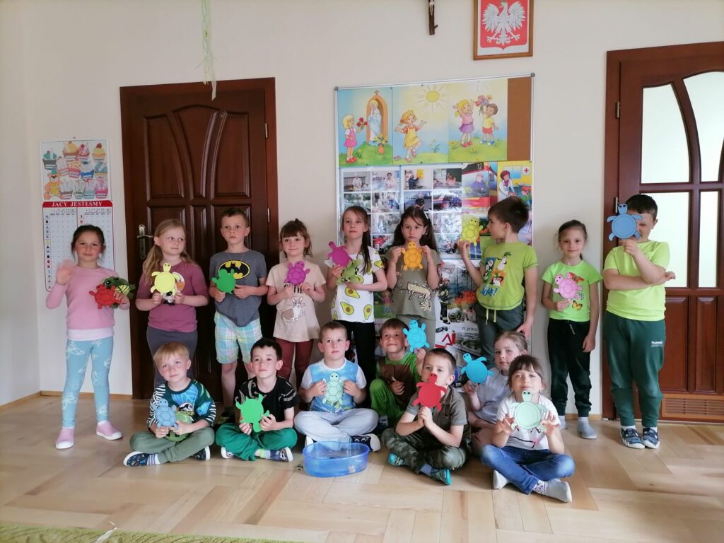 Na zdjęciu widoczna jest grupa przedszkolaków pozujących do wspólnego zdjęcia. Przedszkolaki trzymają w dłoniach kolorowe żółwie z papieru.