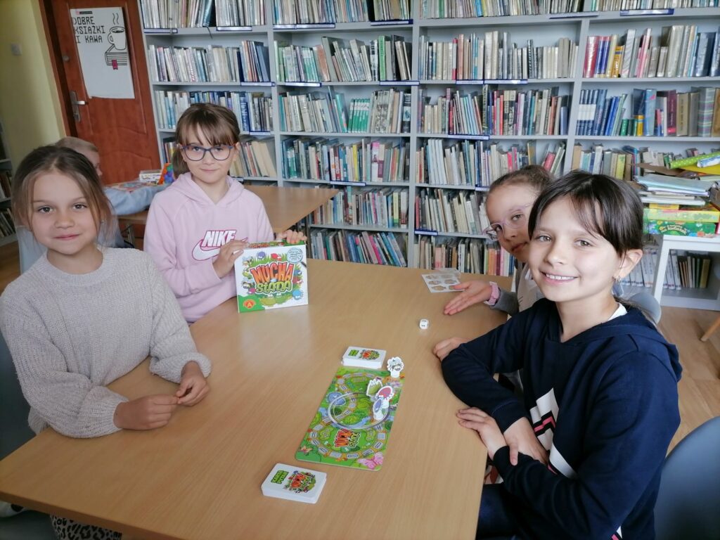 Na zdjęciu widoczna jest grupa 4 dziewczynek pozujących z grą "Mucha nie siada".