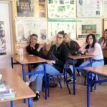 na zdjęciu widać stojącą bibliotekarkę oraz siedzące w ławkach osoby