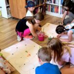 na zdjęciu widać rysujące na kartach rozłożonych na podłodze w sali bibliotecznej
