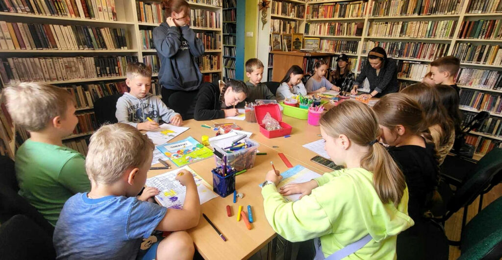 na zdjęciu widać widać dzieci siedzące wokół stołu i rysujące