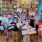 na zdjęciu widać dzieci w sali bibliotecznej trzymające obrazki przez siebie wykonane