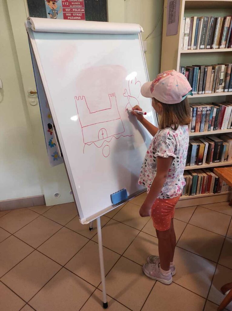 na zdjęciu widać dziecko, stoi przy tablicy, rysuje hasło podczas gry w kalambury