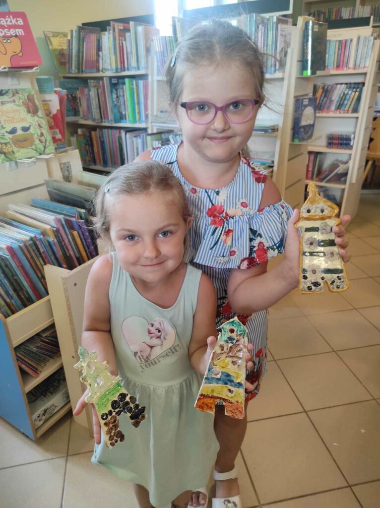 na zdjęciu widać salę biblioteczną, dzieci prezentują prace plastyczne