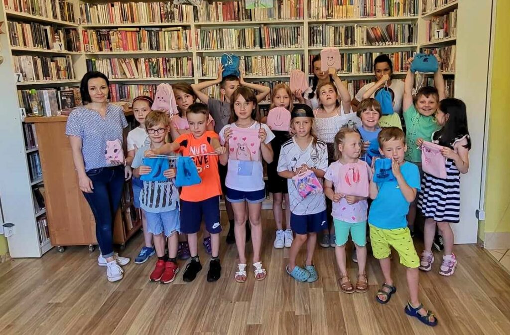 na zdjęciu widać dzieci stojące w bibliotece na tle regałów z książkami