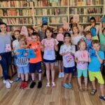 na zdjęciu widać dzieci stojące w bibliotece na tle regałów z książkami