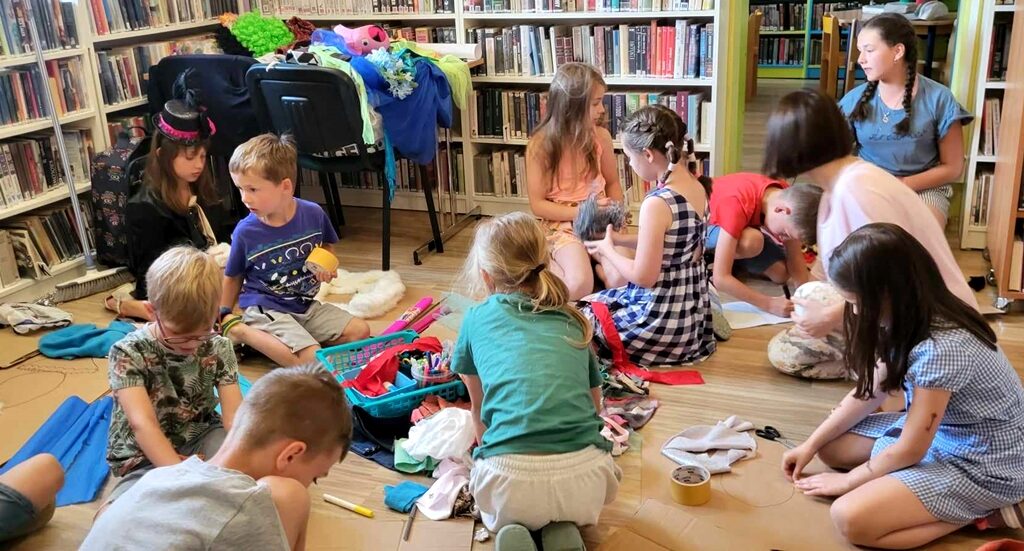 na zdjęciu widać dzieci siedzących na podłodze wśród ścinków tkanin.