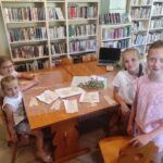 na zdjęciu widać salę biblioteczną, dzieci siedzą przy stole, wykonują pracę plastyczną