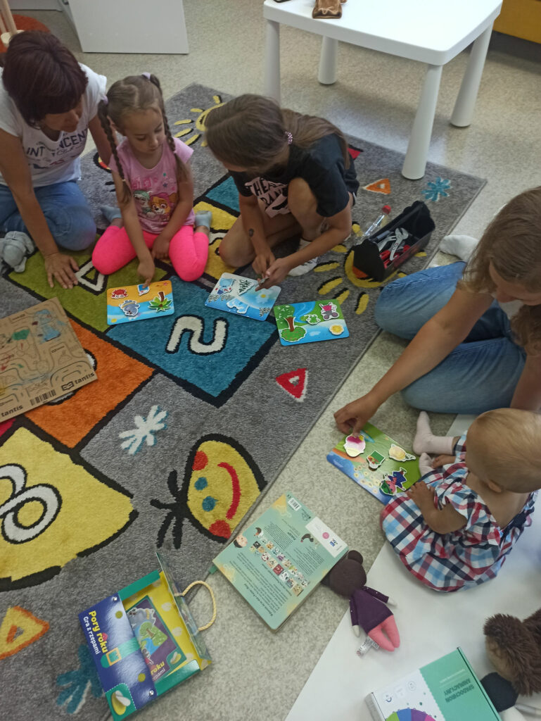 Na dywanie siedzą dzieci wraz z mamamiiukładają kolorowe puzle