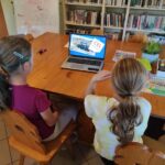 na zdjęciu widać dzieci siedzące przy stole, oglądają film edukacyjny