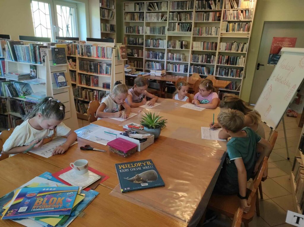 na zdjęciu widać salę biblioteczną, przy stole siedzą dzieci