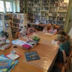 na zdjęciu widać salę biblioteczną, przy stole siedzą dzieci