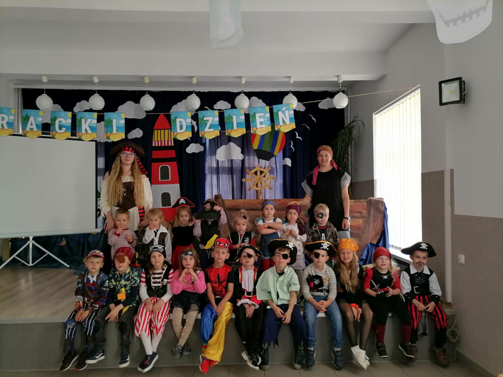 na zdjęciu widoczna jest grupa przedszkolaków z Gminnego przedszkola w Tyliczu wraz z wychowawcami pozujący do wspólnego zdjęcia. W tle piracki statek i latarnia morska.