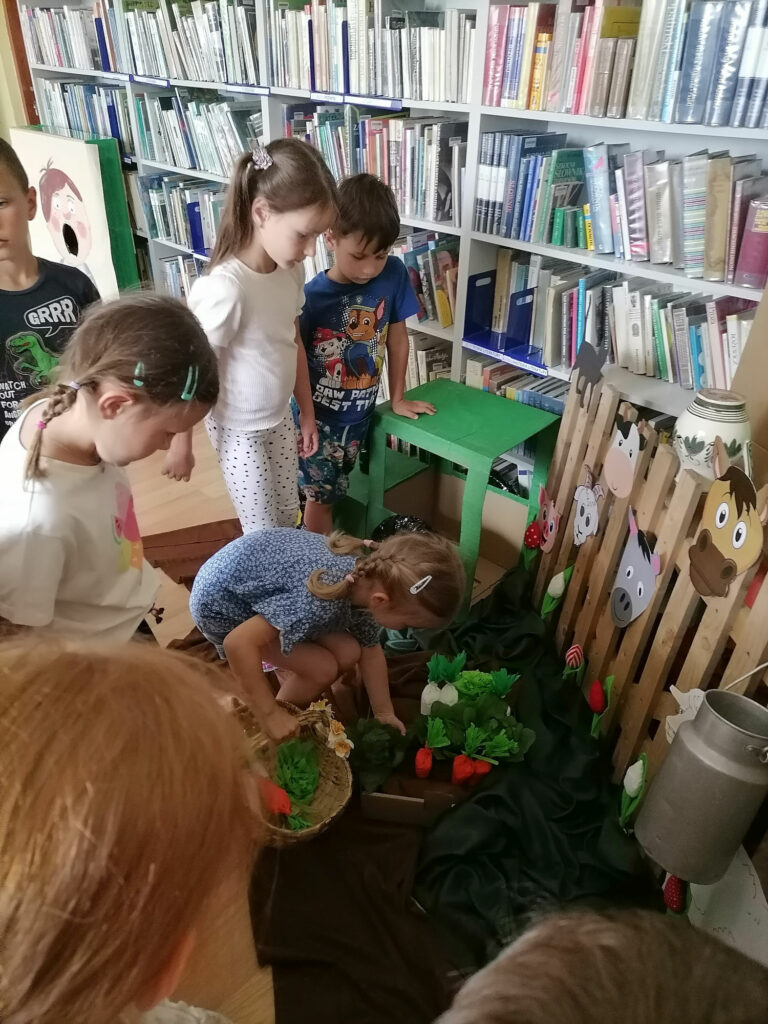 Na zdjęciu widoczna jest grupa dzieci podczas zbierania papierowych warzyw z symbolicznego ogródka.
