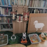 Na zdjęciu widoczna jest przygotowana dekoracja, która stanowiła element zabaw podczas zajęć są to: kartonowe drzwi od stajni z 3 głowami koni, owca oraz plastikowe miski z umieszczonymi w nich słojami do których przymocowane są głowy zwierząt oraz produkty, którymi trzeba te zwierzęta symbolicznie nakarmić.