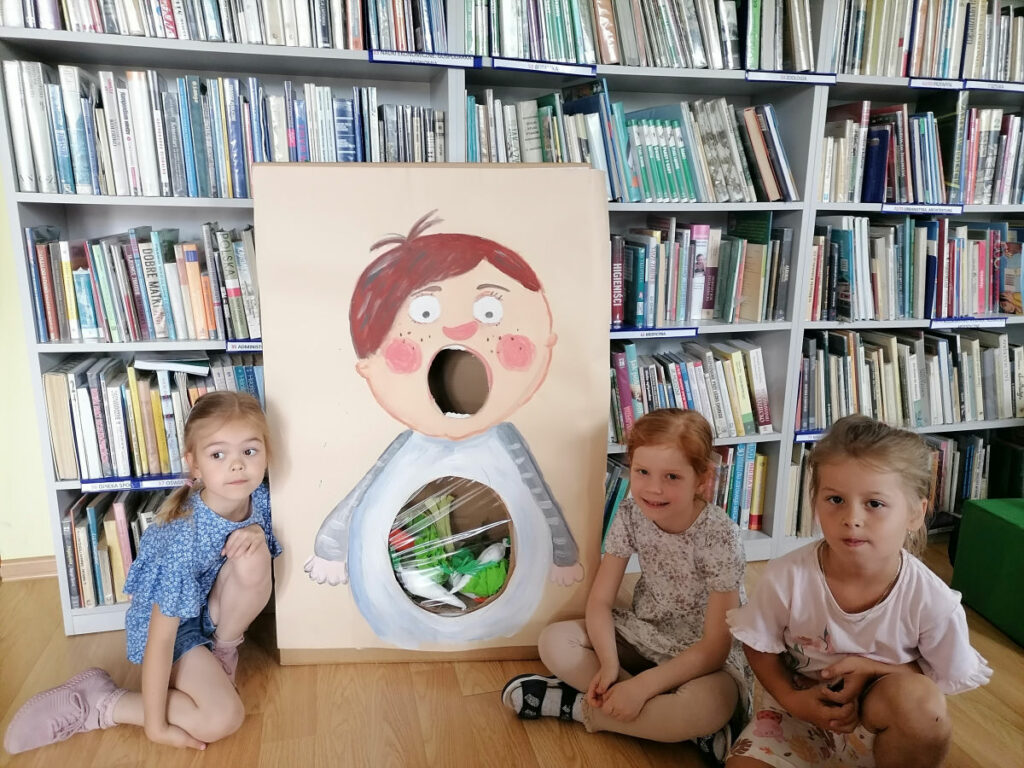 Na zdjęciu widoczne są 3 dziewczynki siedzące na podłodze i pozujące z nakarmionym Puciem.